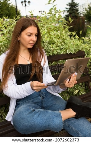 Young beautiful woman works for a laptop in the park. Distant work.	