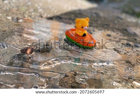 Yellow toy bear on the boat is frozen in a puddle. Forgotten toy in early autumn morning