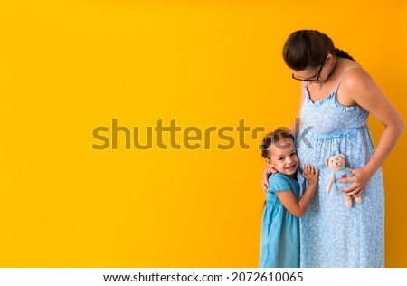 Motherhood, love, Childhood, pregnancy, hot summer - Banner pregnant unrecognizable mother woman expecting baby blue dress lillte Daughter girl sibling teddy bear hug mum belly on yellow background