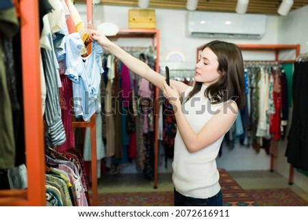 Beautiful female customer taking a picture at the clothes and texting to a friend on her smartphone while at the fashion boutique