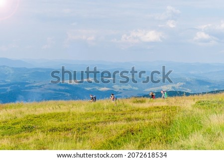 Hiking in the mountains. Tourists go hiking. Green mountains tops, landscape  overgrown with grasses and flowers. Beautiful green mountain scenery  covered with lush vegetation and forest on hills.