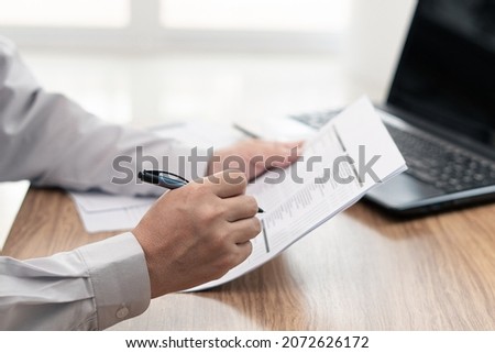 A man use pen write on the checklist paper check service list in office with repair part of car and laptop computer on wood table