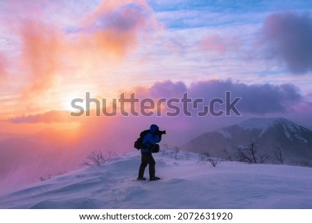 Amazing sunrise. Winter morning. Natural landscape with beautiful sky and cloud. Photographer stays on a meadow covered with snow and takes pictures. High mountain. Snowy background.