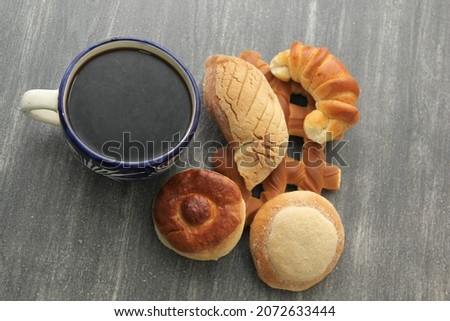 Hot coffee in a blue artisan cup accompanied by delicious, fresh and fluffy Mexican sweet bread: biscuit, croissant, grill, pancha eye and worm
