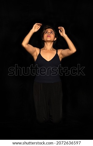 Portrait of a Latin woman with arms raised and looking up on a black background. Female body expression concept.