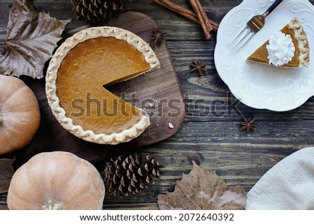 Flatlay of fresh baked pumpkin pie with slice on a plate over wood table background. Thanksgiving Day table. Top view.