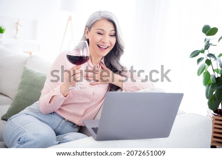 Photo of positive attractive nice old lady sit sofa drink wine talk computer online indoor inside house home