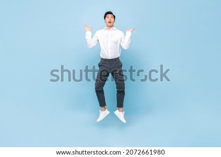Young Asian man jumping with open palms and looking up in isolated light blue color background Royalty-Free Stock Photo #2072661980