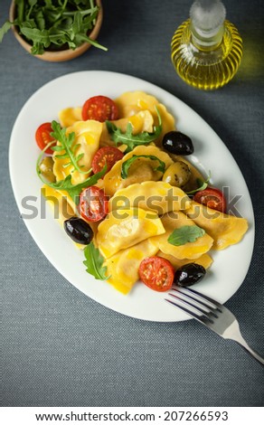 Italian ravioli pasta with olives, tomato and fresh rocket leaves served with a decanter of virgin olive oil as a dressing, overhead view on an oval platter