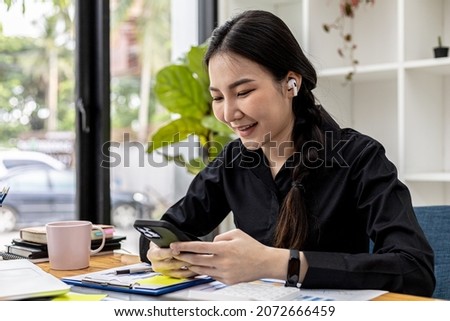 Businesswoman holding smartphone on desk with documents placed, she is looking at data from mobile phone and using a messaging program to talk to business partners. The concept of using technology.