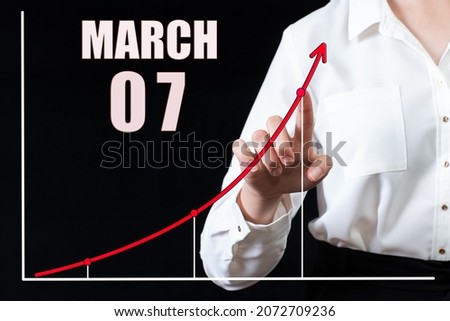7th day of march. Businesswoman's hand pointing to the graph and a calendar with the date of 7 march. Business goals for the day. Spring month, day of the year concept.