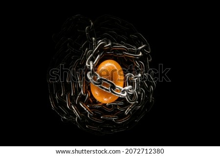 a brown chicken egg entangled in a heavy metal chain on a black background. Conceptual contrast photography about the fragility and resilience of the universe. Comparison of opposites.