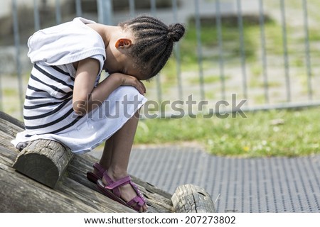 Young girl sitting in a playground in the day with her face in her lap because she is sad Royalty-Free Stock Photo #207273802