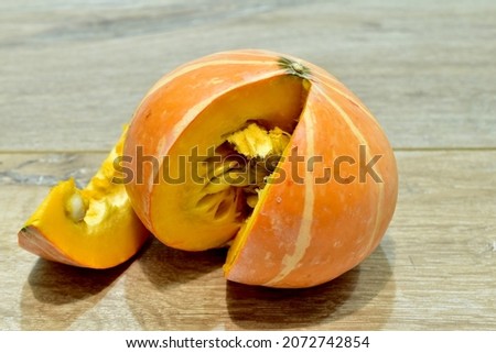 The picture shows a ripe orange pumpkin with a cut slice on a wooden table.