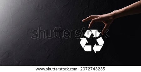 Businessman in suit over dark background holds an recycling icon, sign in his hands. Ecology, environment and conservation concept. Neon red blue light.