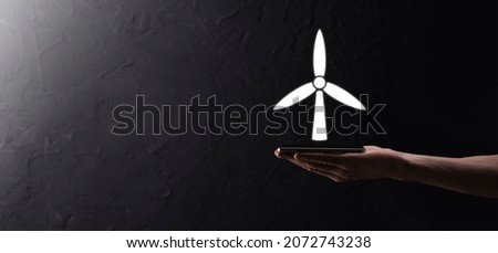 Businessman holding an icon of a windmill that produces environmental energy