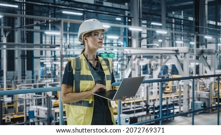 Portrait of Female Automotive Industry 4.0 Engineer in Safety Uniform Using Laptop at Car Factory Facility. Happy Assembly Plant Specialist Working on Manufacturing Modern Electric Vehicles. Royalty-Free Stock Photo #2072769371