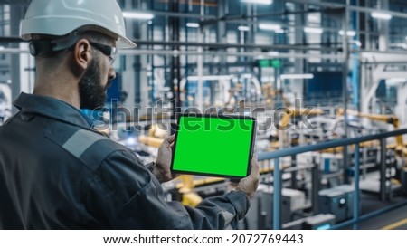 Car Factory Engineer in Work Uniform Using Tablet Computer with Green Screen Mockup Display. Augmented Reality Software at Automotive Industrial Manufacturing Facility Working on Vehicle Production.