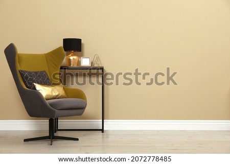 Armchair and console table near beige wall in room, space for text. Interior design