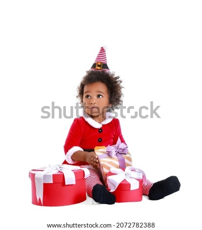 Cute African-American baby girl dressed as Santa and with Christmas gifts on white background