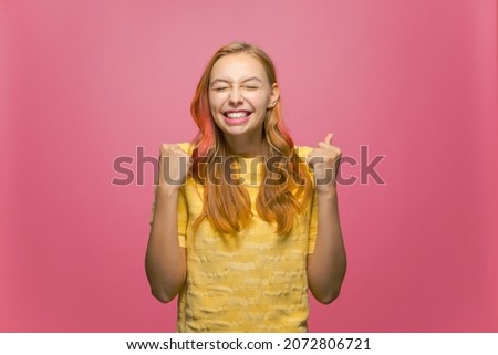 Overjoyed lucky young girl winner feeling triumph, rejoicing raising hands with closed eyes from joy on pink background