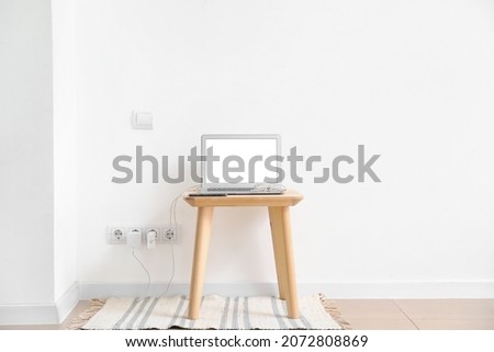 Table with charging laptop and mobile phone near light wall Royalty-Free Stock Photo #2072808869