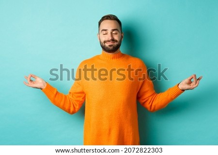 Image of relaxed and relieved man close eyes and smiling, feeling stress-free, meditating with calm expression, standing over light blue background