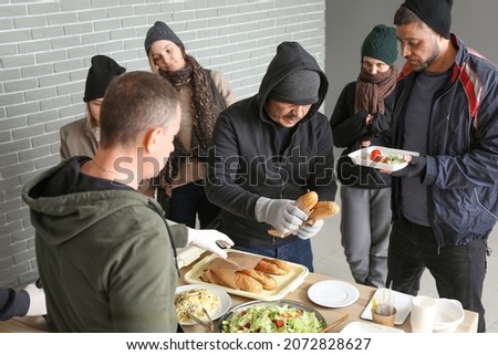 Volunteer giving food to homeless people in warming center Royalty-Free Stock Photo #2072828627