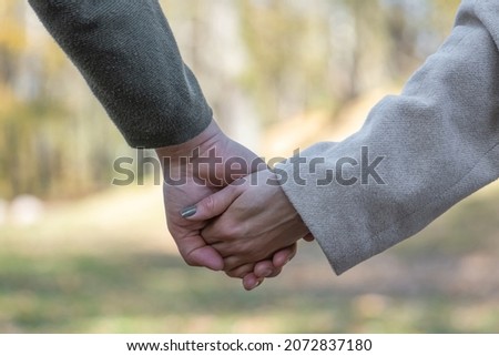 Love, relationship, nature concept. Close-up shot of man and woman holds each other hands in blurred nature background during cold and sunny day