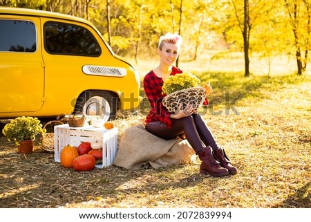 beautiful woman with flowers and pumpkins in autumn park background near yellow car