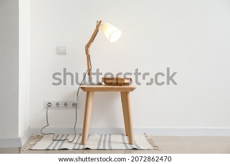Glowing lamp and books on table near light wall Royalty-Free Stock Photo #2072862470