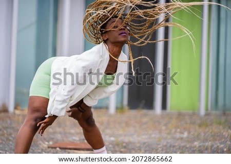 Photo with copy space of a black woman with braids dancing freestyle in front of a modern building