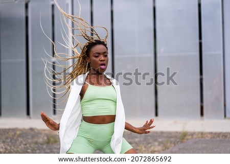 Photo with motion of an african young woman with braids dancing with energy in an urban landscape