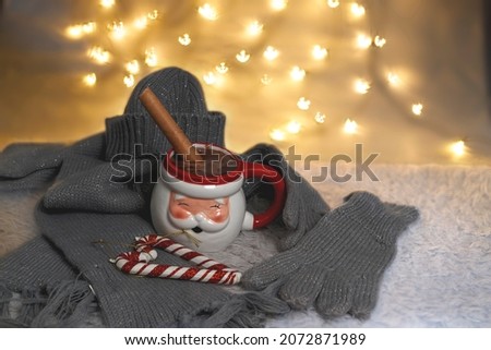 Chocolate mug in the shape of Santa Claus accompanied by hat, gloves, scarf and Christmas sticks on defocused bokeh background