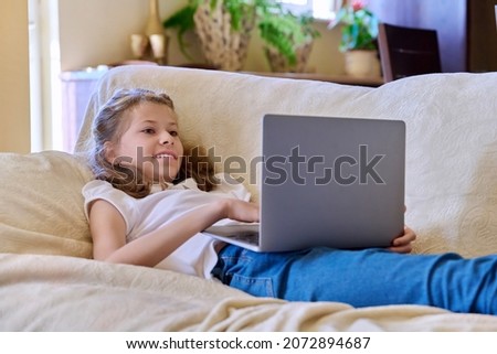 Child girl with laptop at home on the couch