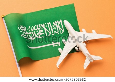 Saudi Arabia flag and toy plane on orange background, concept on the theme of travel to the country