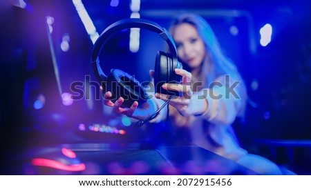 Woman hand hold headphones with microphone for video games and cyber sports on neon background banner.