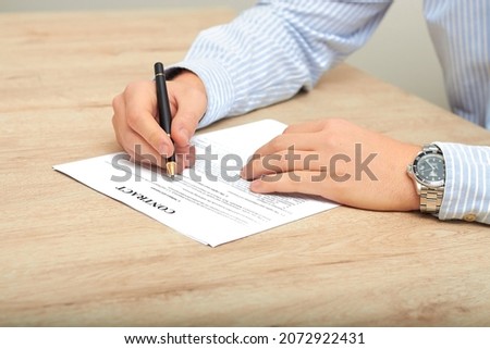 A man signs a document with a pen on the table at home. The businessman signs, puts signatures on the document. work from home, remote work, business concept. the guy is an online learning student.