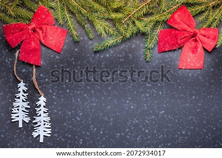 two white Christmas tree toys in the form of Christmas trees, two large red bows and branches of a real green Christmas tree lie on a black background. Snowflake effect