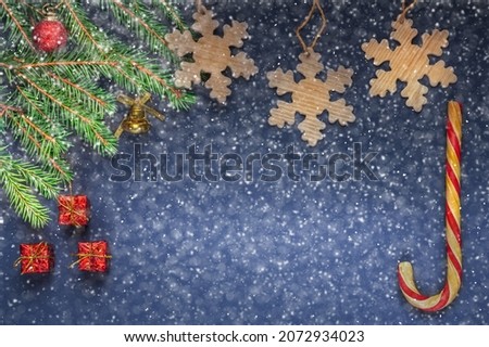 decorated fresh christmas tree, wood snowflakes, christmas candy and three little gifts on dark background with a lot of white snowflakes or snow