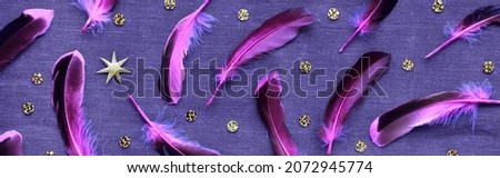 Scattered pink purple feathers. Canvas linen background with the feathers, gold stars and golden confetti. Flat lay, vibrant bold neon colors on dark textile background.