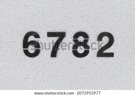 Black Number 6782 on the white wall. Spray paint. Number six thousand seven hundred and eighty two.