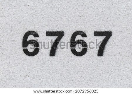 Black Number 6767 on the white wall. Spray paint. Number six thousand seven hundred and sixty seven.