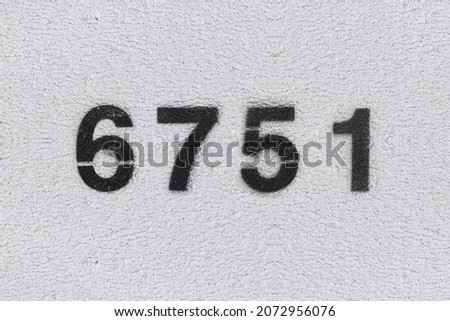 Black Number 6751 on the white wall. Spray paint. Number six thousand seven hundred fifty one.