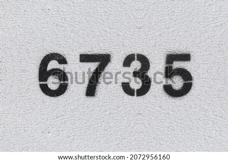 Black Number 6735 on the white wall. Spray paint. Number six thousand seven hundred thirty five.