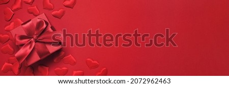 Valentines Day festive banner, gift box with ribbon and satin hearts on red, copy space