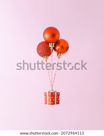 Creative composition with levitating three red Christmas decorations and giftbox. Trendy holiday shopping concept.