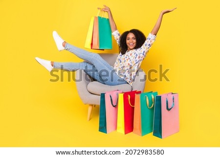 Full body photo of sweet young wavy hairdo lady sit on armchair with bags wear shirt jeans sneakers isolated on yellow background Royalty-Free Stock Photo #2072983580