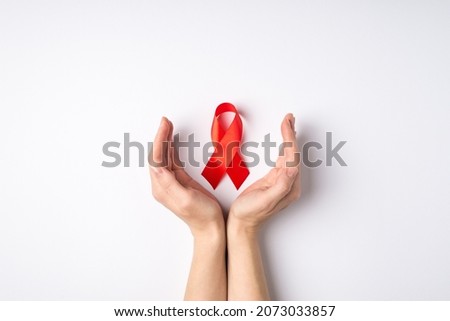 First person top view photo of cupped female hands and red ribbon symbol of aids awareness on isolated white background