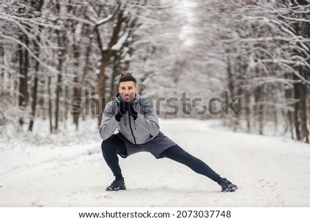 Fit sportsman doing stretching and warmup exercises in forest at snowy winter day. Healthy life, warmup, cold weather Royalty-Free Stock Photo #2073037748